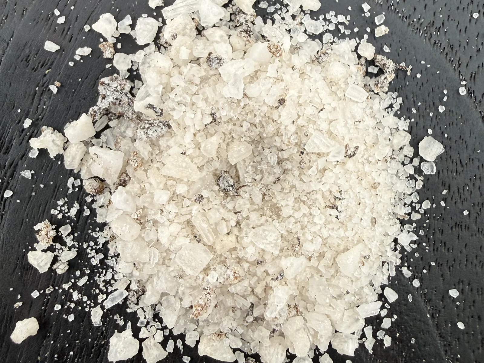 Coarse white sea salt mixed with visible brown mushroom pieces on dark wood