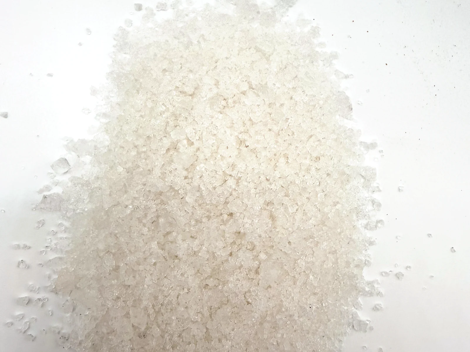 A heap of fine, irregular white fleur de sel crystals photographed from above on white