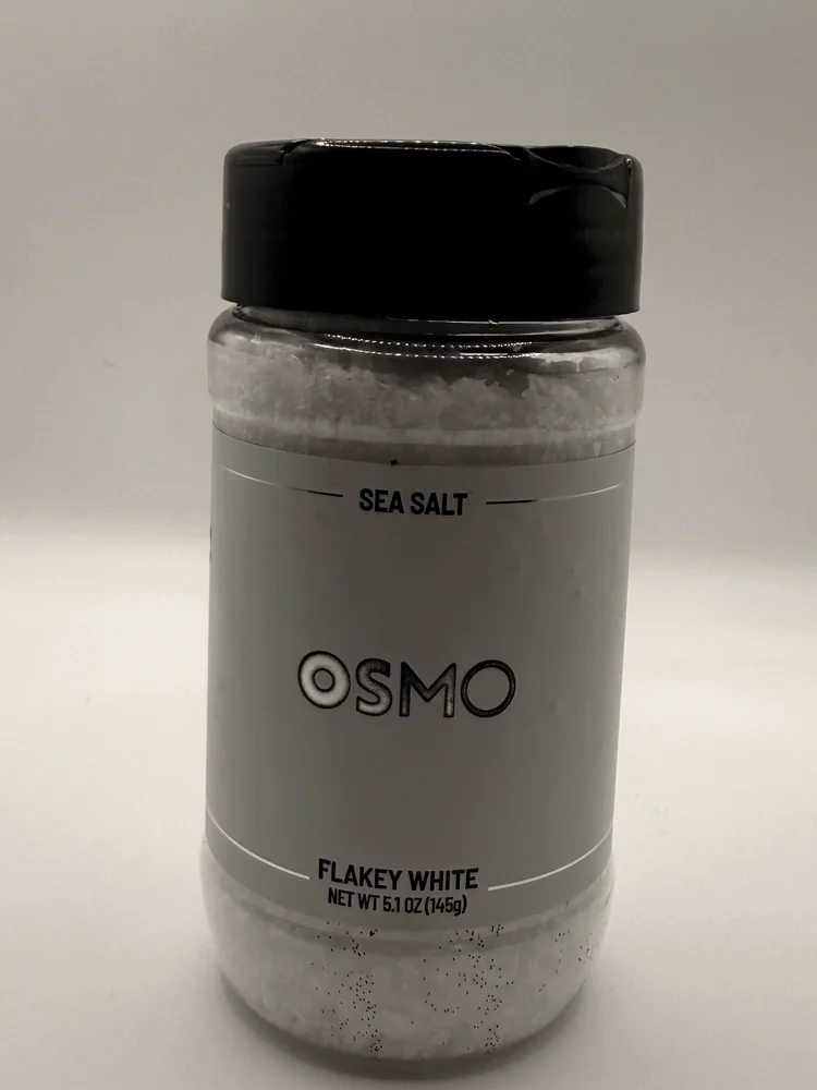 Clear plastic jar of OSMO Flakey White Sea Salt with a grey label and black lid