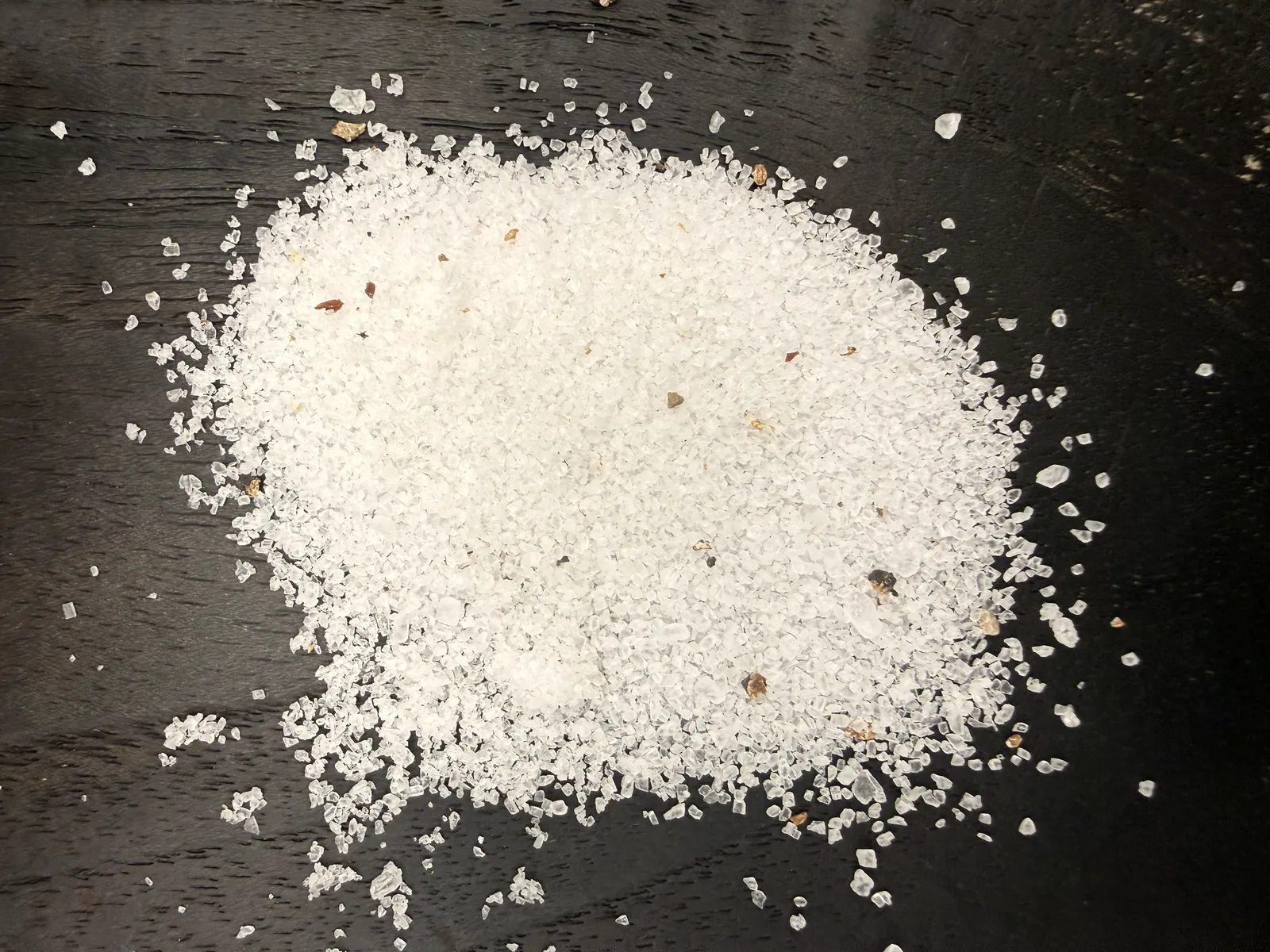 Coarse white sea salt mixed with scattered brown and black truffle pieces on dark wood
